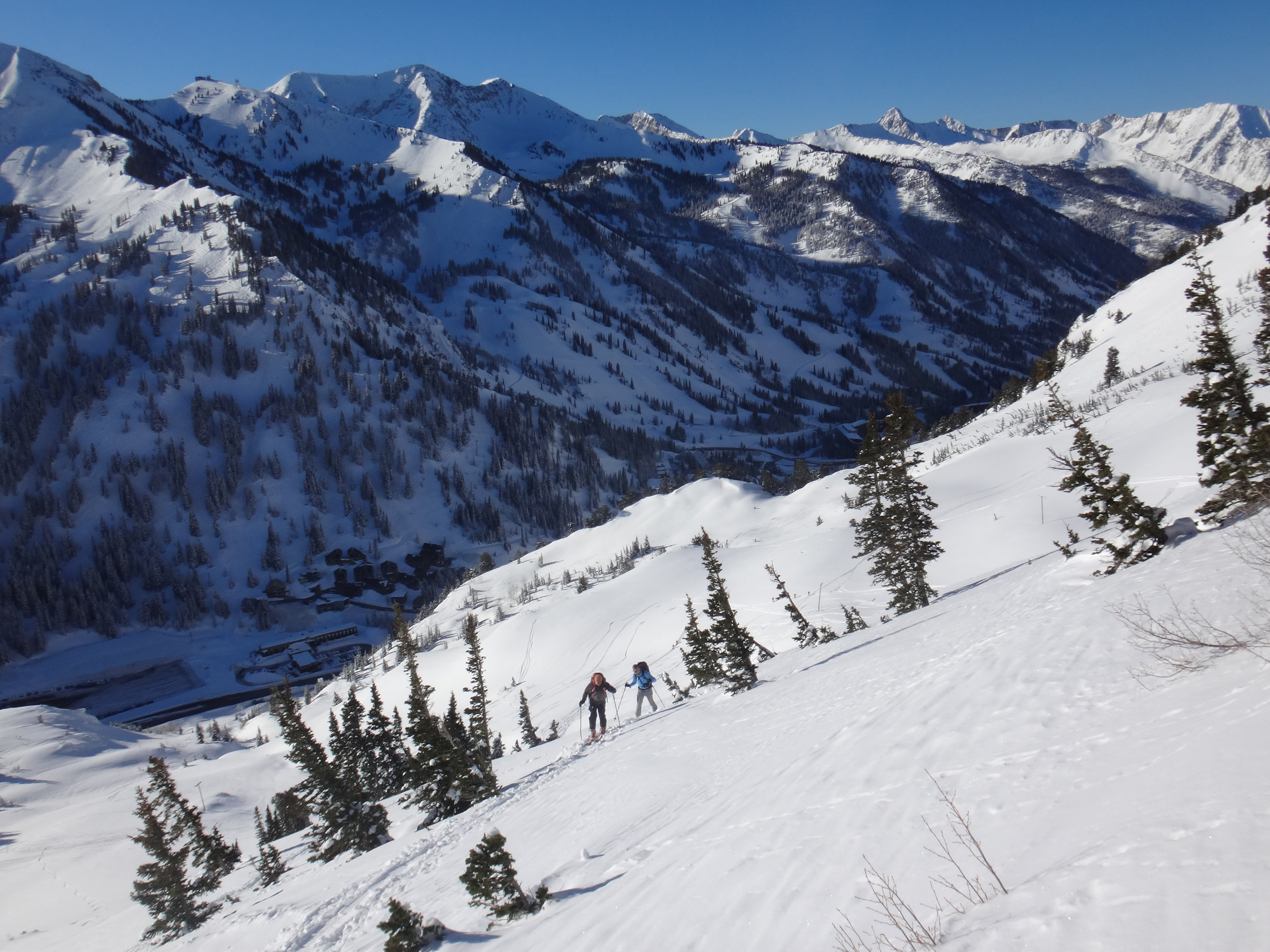Two ski tourers skinning a sunlit slope above a mountain range