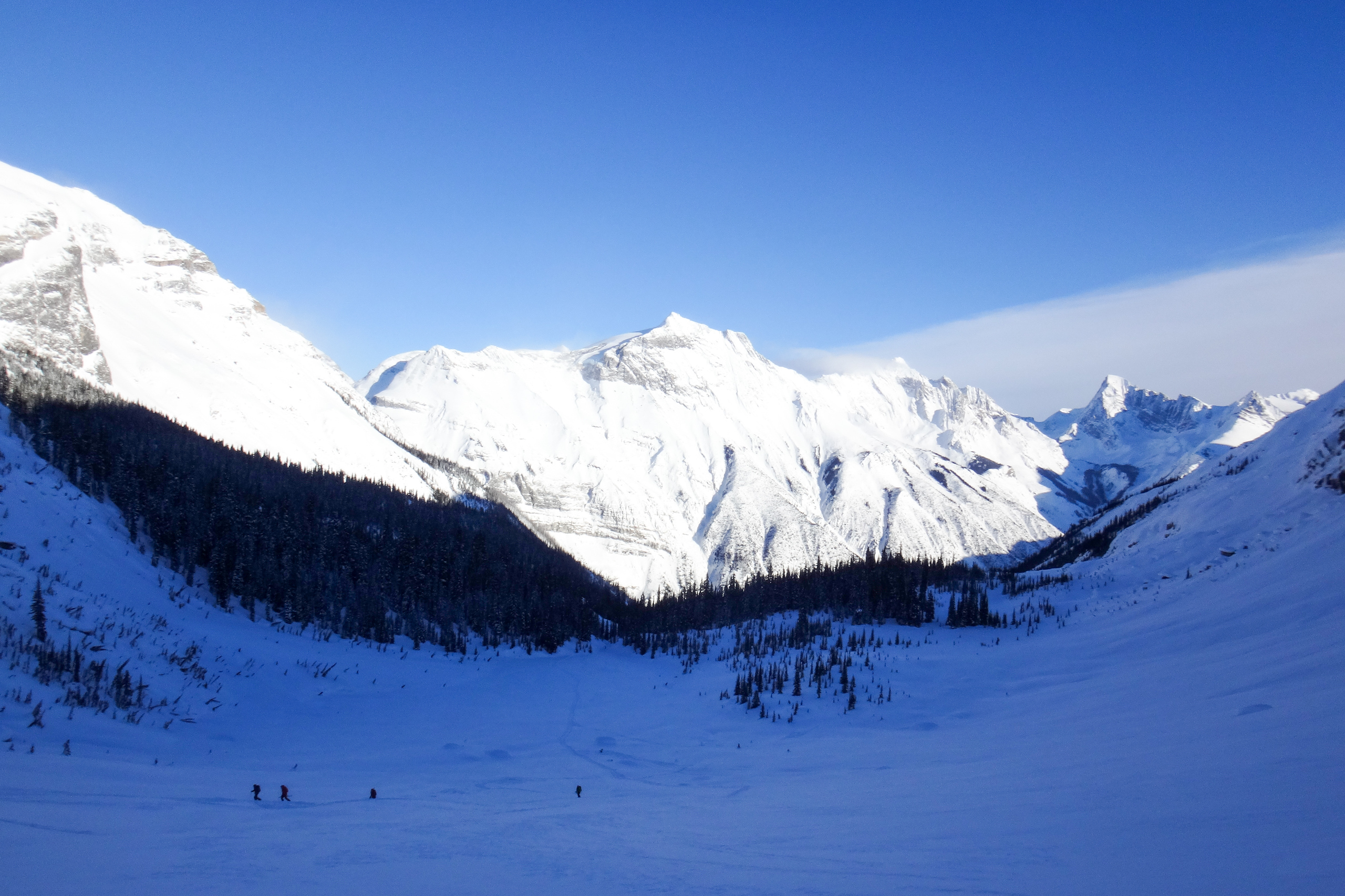 Ski tourers crossing a shadowed basin toward sunlit peaks