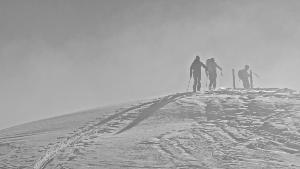 Three ski tourers on a wind-sculpted snow ridge